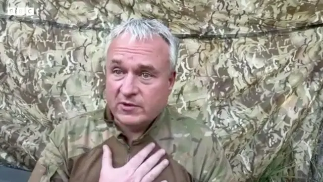 Мужчина в камуфляже прижимает руку к груди