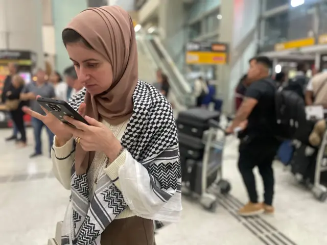 Mulher com véu islâmico olhando para celular em aeroporto
