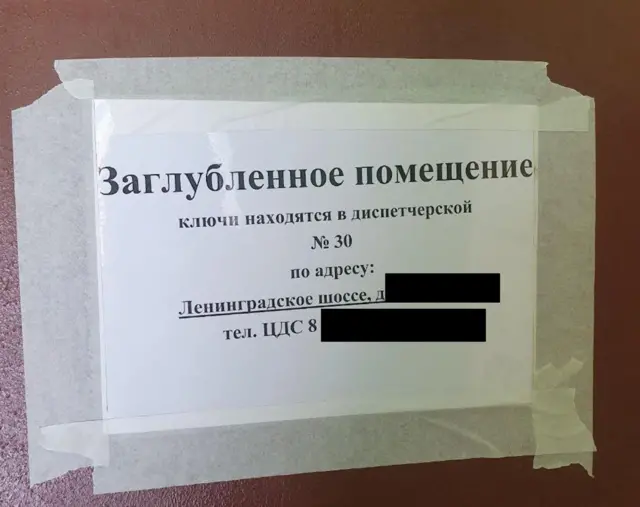 Приклеенный бумажным скотчем лист бумаге. На листе надпись: "Заглубленное помещение. Ключи находятся в диспетчерской №30 по адресу: Ленинградское шоссе". Полный адрес скрыт.