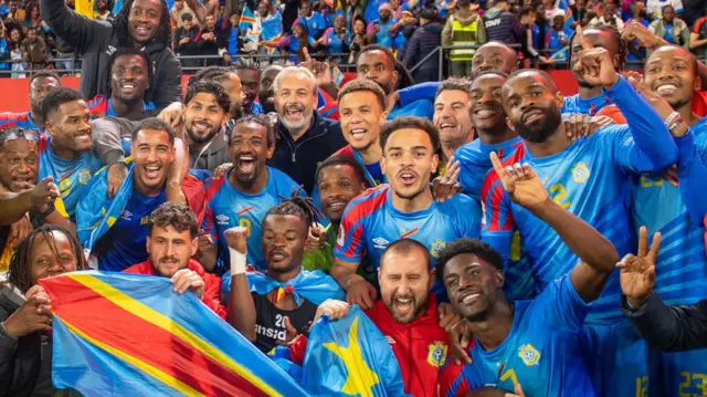 Jogadores e membros da comissão técnica da República Democrática do Congo posam atrás de bandeiras nacionais, comemorando uma vitória