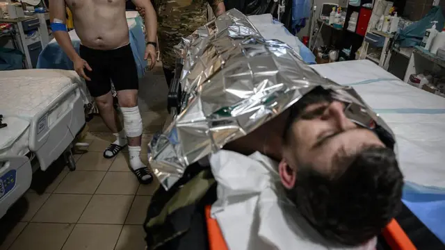 Чоловік лежить накритий покривалом з фольги, на задньому фоні інші поранені