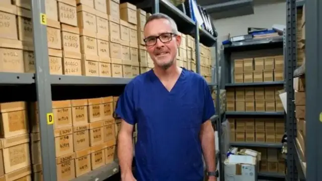 پروفسور کوین موناهان در کنار جعبه‌های نمونه که در قفسه‌ها چیده شده‌اند