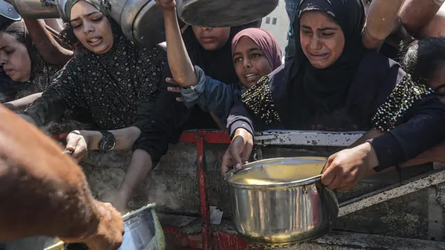 نازحون فلسطينيون، بمن فيهم الأطفال، يحملون أواني الطعام أثناء تلقيهم الطعام من مطبخ خيري في مدينة غزة.