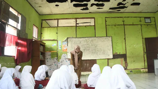 Seorang Guru (tengah) memberikan materi pembelajaran kepada sejumlah siswi SDN (Sekolah Dasar Negeri) Sukadaya 02 tanpa bangku dan meja di Sukawangi, Kabupaten Bekasi, Jawa Barat, Senin (22/8/2022).