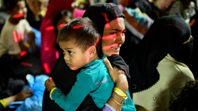 A Rohingya Muslim woman reacts while holding her child, as they are relocated from their temporary shelter in Banda Aceh, Indonesia following protests on 27 December 2023