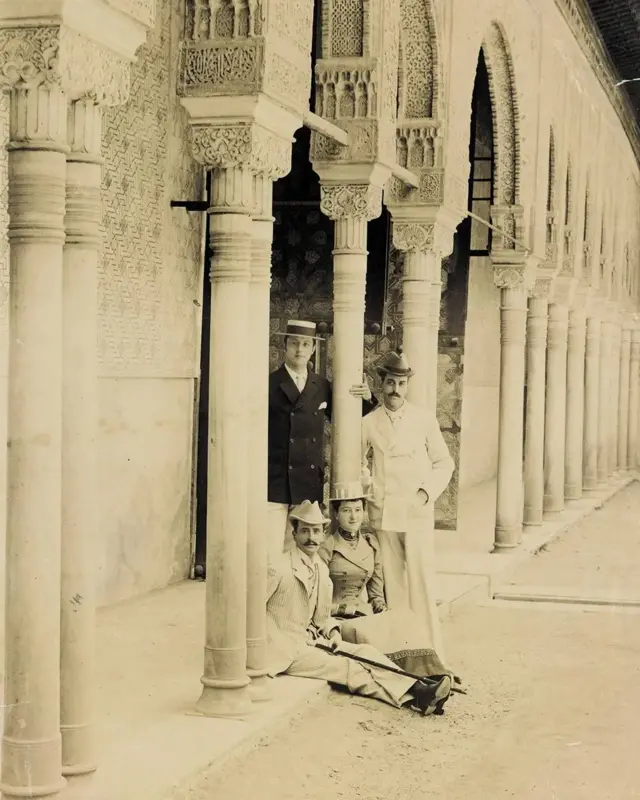 Foto de George W Vanderbilt con amigos en Granada, España. En la imagen se ve a Vanderbilt, dos amigos y una amiga, con atuendos de la época y sombreros, en una antigua construcción con arcos en Granada.
