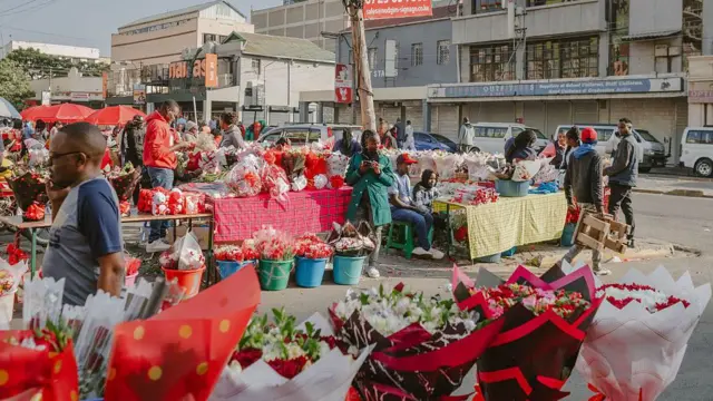 A market stall selling bunches of fresh flowers, with buildings behind it and lots of people milling around.