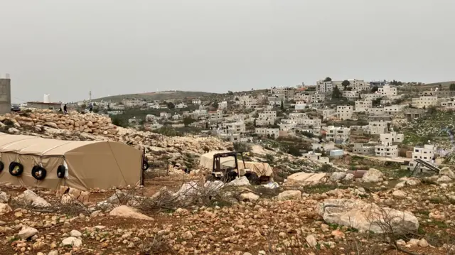 منظر لقرية المغيير، به عشرات المنازل البيضاء المبنية من الطوب الخفيف تنتشر على سفح تل مغطى بصخور بنية وعرة وعشب أخضر.