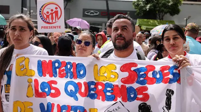 Dört kişi protesto sırasında bir pankart taşıyor. Hepsi beyaz tişört giyiyor.