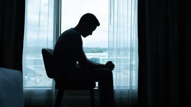 Seorang pria duduk sendiri di dalam kamar.