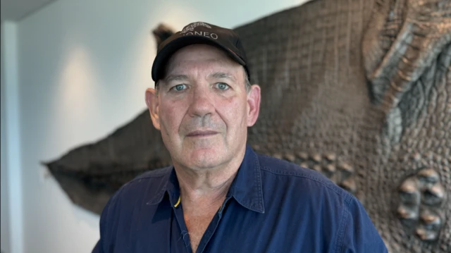 Foto Mick Burns, um homemcasa de aposta com deposito baixopele e olhos claros, usando uma camisa azul-marinho e um boné. 