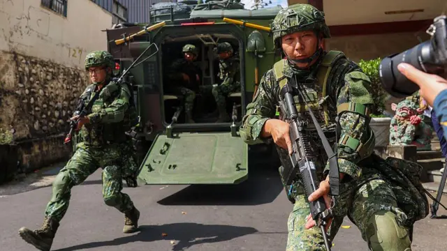 Двоє тайванських солдатів вистрибують з військової машини, тримаючи гвинтівки, під час військових навчань у Тайчжуні