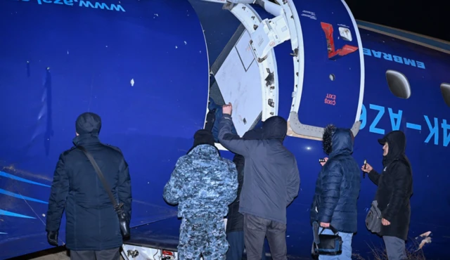 Kazak yetkililer uçağın dış cephesinde inceleme yapıyor, üzerlerinde kalın montlar var. 