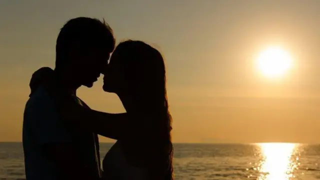 Sahilde batan güneşe karşı birbirine sarılan bir çiftin silüeti