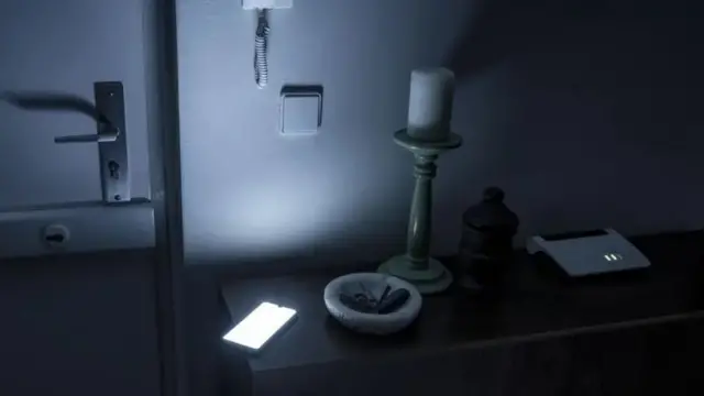 අඳුරු පරිසරයක මේසයක් මත ඇති Wifi උපාංගයක් සහ ජංගම දුරකතනයක්