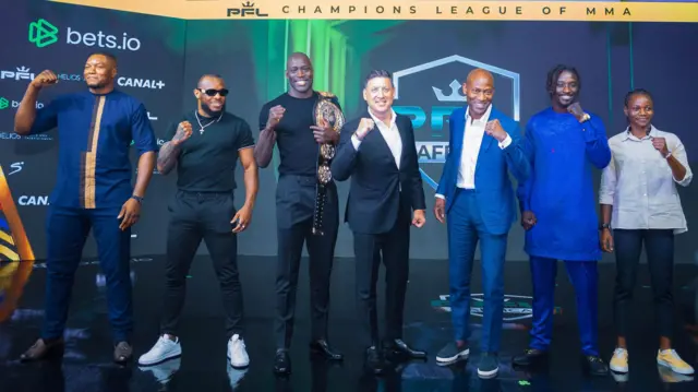 Une photo montrant des combattants de la PFL Africa qui étirent leurs poings droit et gauche en souriant, l'un d'entre eux tenant une ceinture sur son épaule gauche.