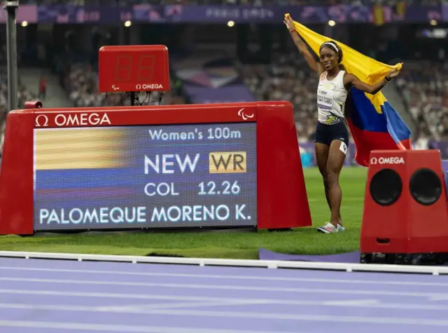 La colombiana Karen Palomeque al costado de una pantalla que muestra su récord mundial en 100 metros femenino, categoría T38 (personas con algún tipo de dificultad de movimiento y coordinación).