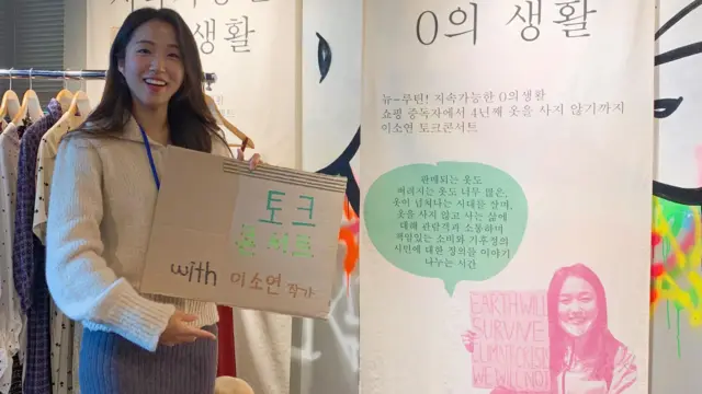 她手上拿著一張用回收紙箱製成的海報，上面寫著：「作家李素妍談會」。