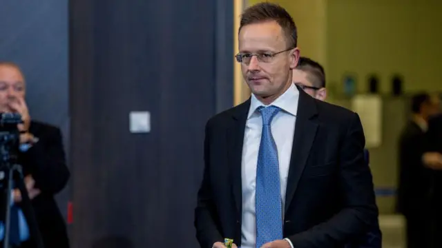 Петер Сіярто іде в костюмі та краватці в якомусь залі