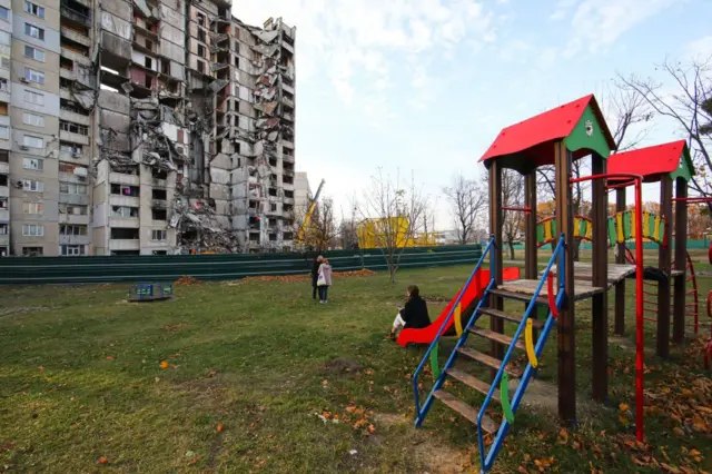 Niños ucranianos en un parque frente a un edificio derruido
