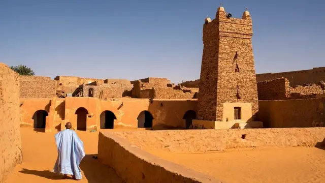 مئذنة مسجد شنقيط العتيق ورجل يرتدي عباءة زرقاء اللون 