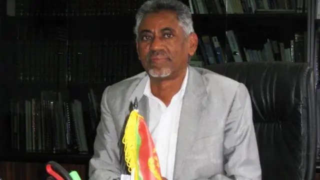 ምኒስተር ዜና ኤርትራ የማነ ገብረመስቀል ኣብ ቤትጽሕፈት ኮፍ ኢሉ ካሜራ እናጠመተ፡ ኣብ ቅድሚኡ ባንዴራ ኤርትራ ትርአ