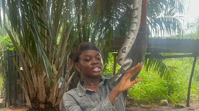 Girl hold snake wit palm tree for di back