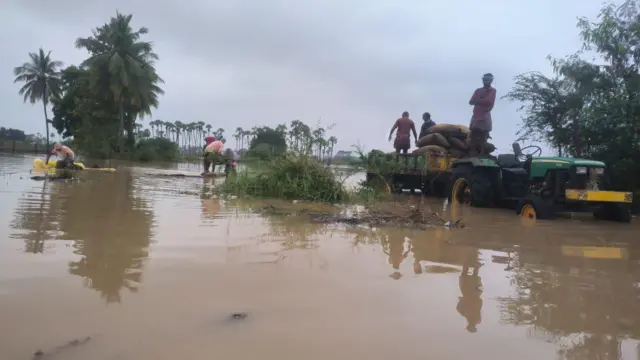వరదలో చిక్కుకున్న ధాన్యాన్ని తరలిస్తున్న రైతులు 
