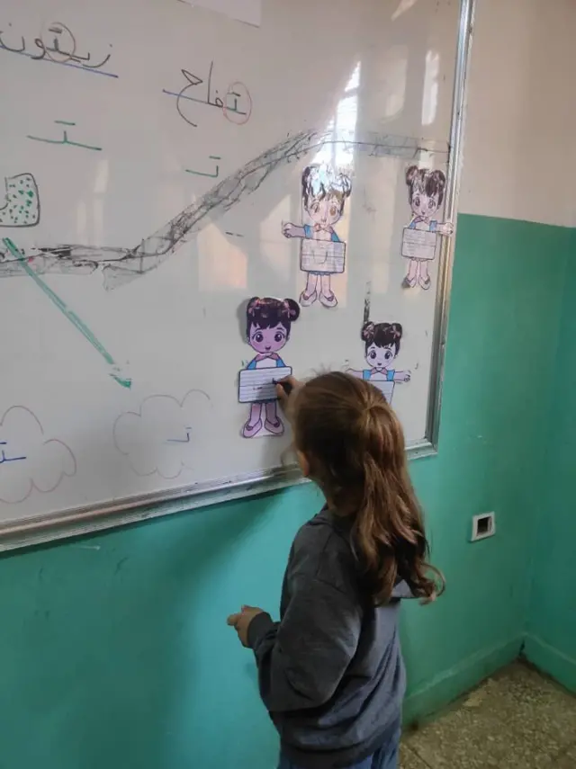 Suriyeli bir kız çocuğu tahtaya yazı yazıyor.