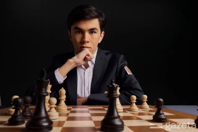 Ўзбекистонлик гроссмейстер Жавоҳир Синдаров, ўтирган ҳолатда, шаҳмат доскаси ва шаҳмат доналари унинг олдги фонида