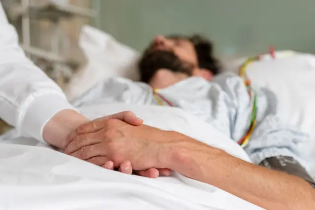 Paciente en cama con la mano entrelazada a la de otra persona