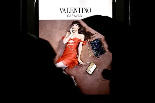 Valentino Garavani markasına ait bir reklam panosunda kırmızı elbiseli bir model telefonla konuşurken poz vermiş.