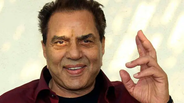Dharmendra raise im hand, e wear wine shirt ande dey smile
