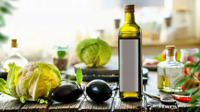 زجاجة تحتوي على زيت الزيتون وبجانبها عدد من الخضراوات