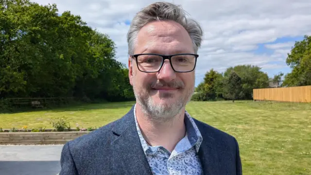 Garet stoji na velikom travnjaku kuće Brinavel u pozadini. 