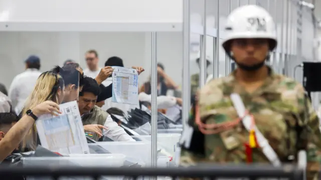 Al fondo se ven trabajadores del Tribunal Electoral haciendo el recuento de votos y en primer plano se ve a un hombre de seguridad cuya imagen está difuminada