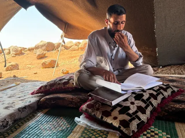 رجل في منتصف العمر يجلس في خيمته يصحح أوراق الامتحانات.