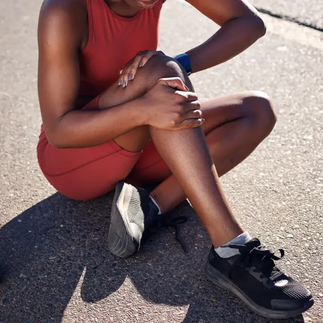 Жінка у спортивній формі сидить на землі і тримає рукою коліно