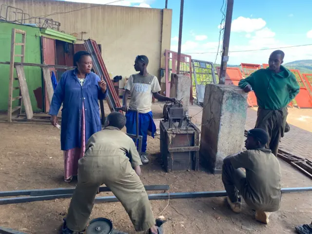 Ifoto igaragaza abantu bane barimo na Françoise Umuhoza. Babiri bari hafi y'icyuma bagiye gusudira, abandi bari ku rundi ruhande ruteganye na bo. Umuhoza ari kubaha amabwiriza y'ibyo bagiye gukora bamuteze amatwi. 