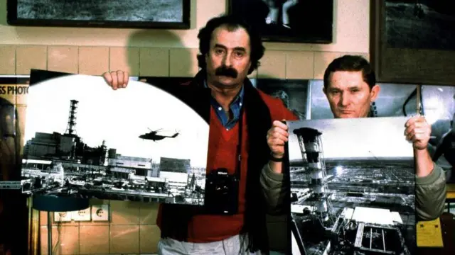 Dos hombres sostienen dos imágenes de la planta de Chernóbil tomadas desde un helicóptero. 