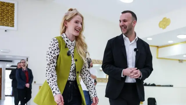 Hannah Spencer ve Green Party leader Zack Polanski ayakta gülümseyerek konuşuyor