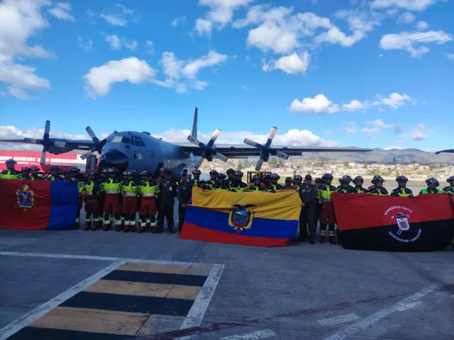 Personal de rescate junto a un avión y una bandera ecuatoriana
