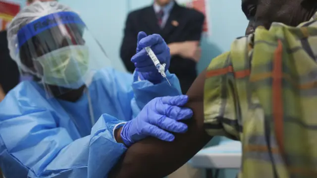 A nurse in blue scrubs, visor and face mask administers an injection on the first day of the Ebola vaccine study being conducted at Redemption Hospital, Monrovia, Liberia - 2015.