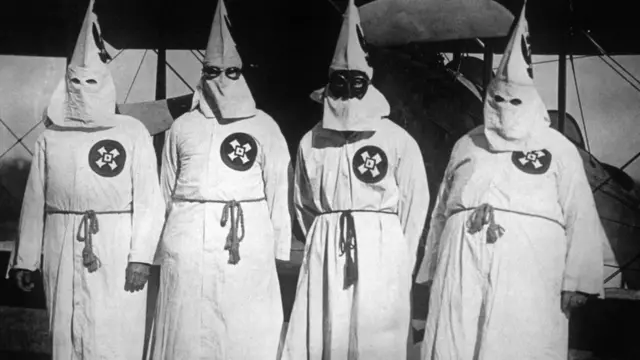 সাদা ইউনিফর্ম পরা কু ক্লাক্স ক্লানের সদস্যরা। কৃষ্ণাঙ্গদের পুড়িয়ে মারতো এরা।