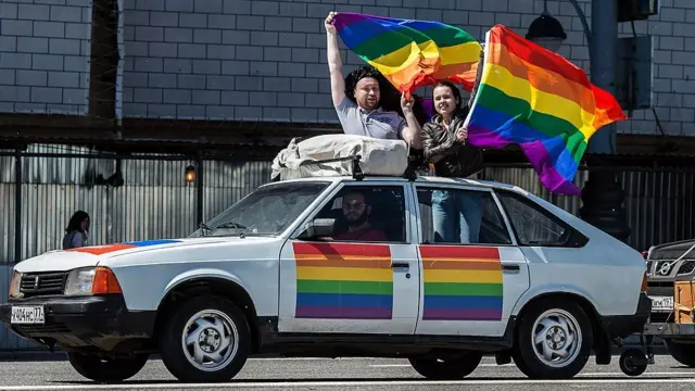 Unos jóvenes con la bandera gay en un coche