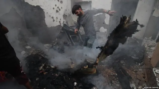 मुठभेड़ के बाद अपने घर का मलबा हटाता एक व्यक्ति