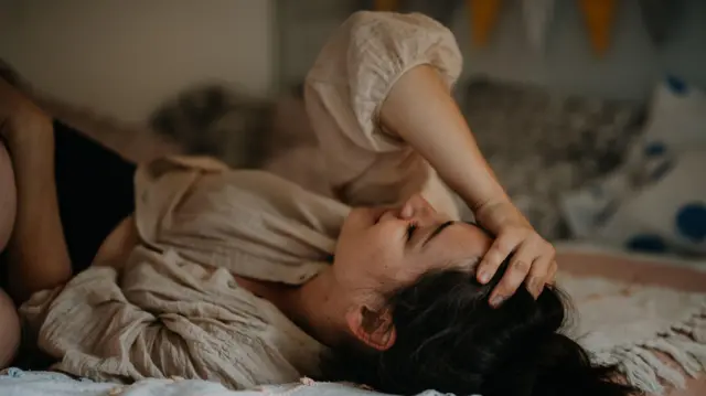 Une femme est allongée sur son lit, la main contre son front.