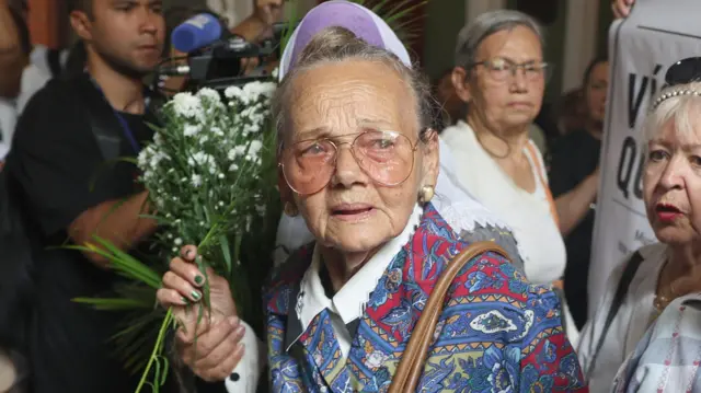 La venezolana Carmen Navas durante una misa en memoria de su hijo en Caracas, con lentes, lágrimas en los ojos y un ramo de flores en sus manos.