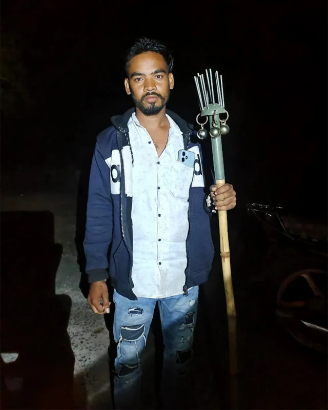 Muškarac tamne kose sa bradom u svetloj košulji, plavoj jakni i u farmerkama drži poseban štap za zaštitu od medveda lenjivaca, koji ima tupe šiljke i zvončiće.