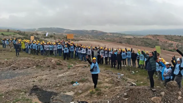 Üstlerine mavi renkte grev yeleği giyen Doruk Madencilik işçilerinin Eskişehir'den Ankara'ya başlattığı yürüyüşte, boş bir arazide mola verdikleri ve kameralara poz verdikleri görülüyor. 